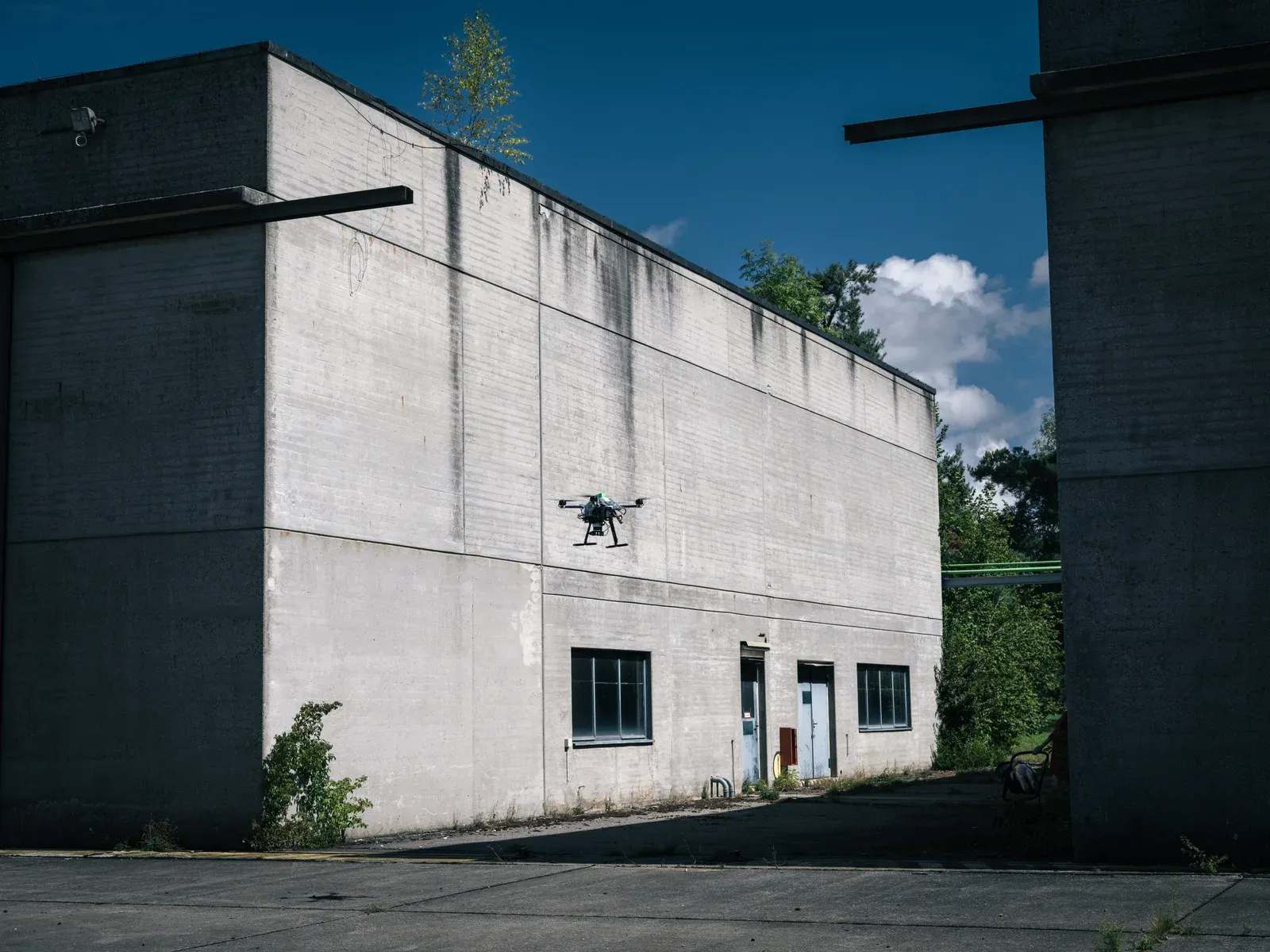 A research quadcopter flying between concrete buildings at the SPRIND competition venue.